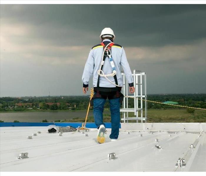 Man on top of a roof, using protective equipment while inspecting roof