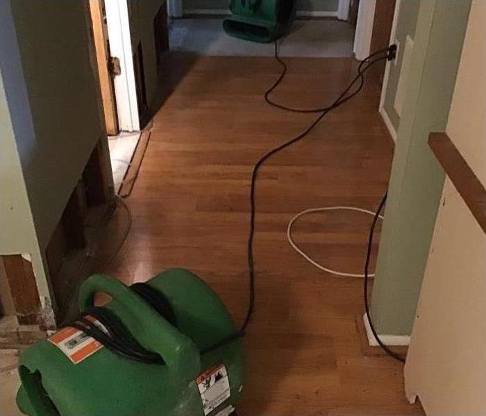 Two air movers placed on baseboards of a wall due to water damage.
